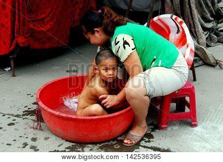 Pengzhou, China - October 5 2007: Mother gives her toddler son a bath in a large plastic pan in front of her clothing shop in Jiu Chi Town