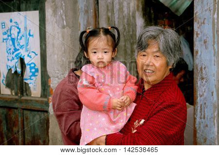 Pengzhou China - September 26, 2006: Grandmother holding her toddler grand daughter in front of their home on Hua Lu (Old Street)