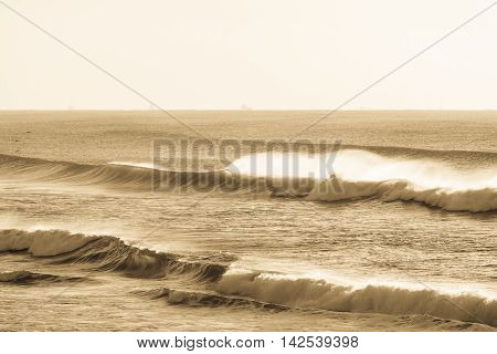 Ocean waves crashing along beach coastline in vintage antique sepia.