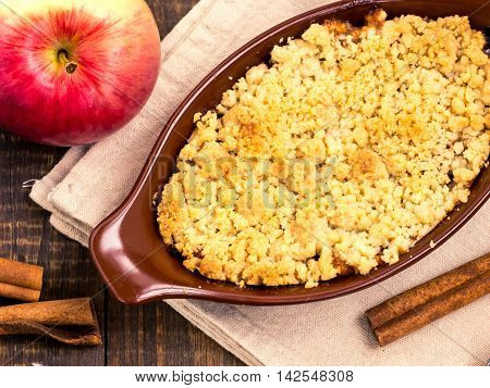 Homemade apple cramble cake with fresh apples and cinnamon sticks on rustic dark wooden background. Top view or flat lay