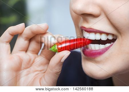 Natural sexy caucasian woman with red hot chili pepper in mouth in a blurry background