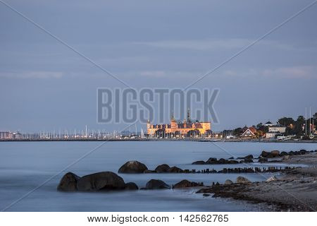 The castle of Prince Hamlet is lit and glows in orange against the blue sky and soft waves of Zealands North coast.