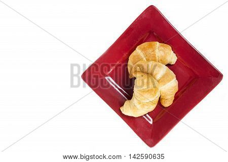 Three fresh flakey buttery croissants on a red plate and isolated on white with copyspace.