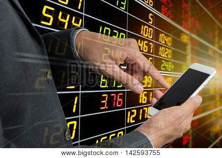 Businessman's hand using smart phone with display board of Stock market quotes in background.