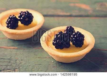 Homemade round tartlets with lemon curd and fresh blackberries on wooden table