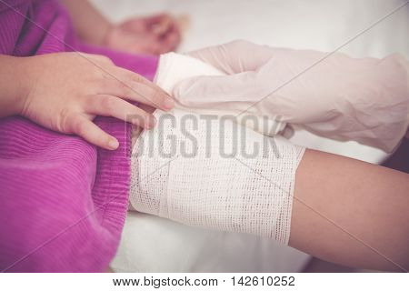Child Injured. Pediatrician Doctor Bandaging Child's Knee. Vintage Tone Effect.