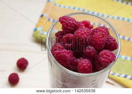 Simmer fresh raspberries in a glass on a wood and yellow background