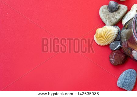 Red summer background with sea pebbles shells and a glass; place for text.