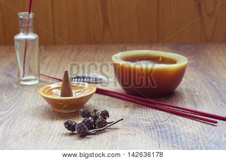 Aromatherapy still life with candle bottle aromastick and incense cone in a ceramic stand on a wooden table.