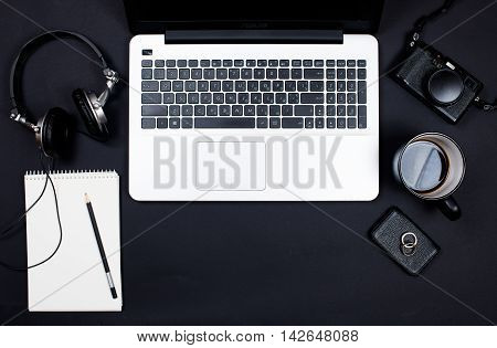 Businessman desk workspace with laptop keyboard, retro camera, headphones and notepad on black background. Startup concept, top view mockup.