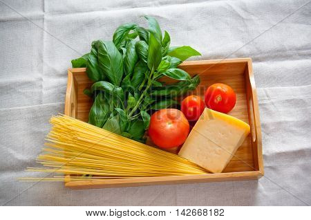 Green basil chunk of parmesan cheese raw cappellini and tomatoes on wooden tray