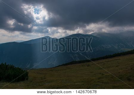 Beam of light shining through a hole in the clouds over a mountain landscape