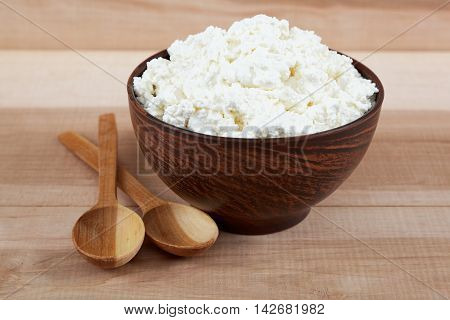 Fresh cottage cheese in a bowl with spoon on a wooden table.