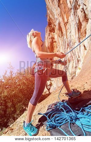 Blond Female Athlete belaying her Climbing Partner with Rope staying at orange rocky overhanging wall blue Sky and shining Sun