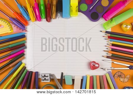 Different school supplies are on white blank notebook.