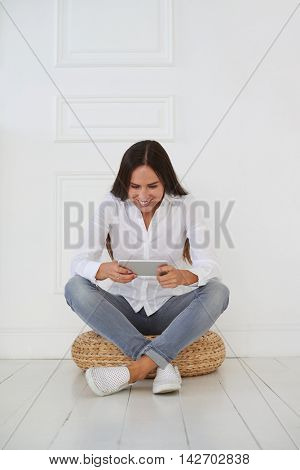 An attractive brunette sitting on a hassock using a digital tablet