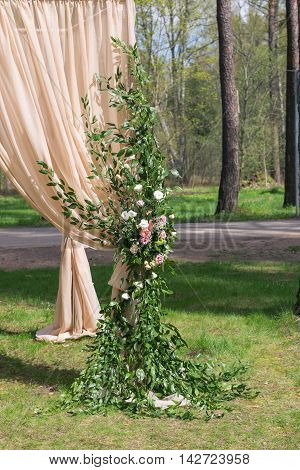 Beige wedding arch decorated with flowers, stands on a beautiful green lawn