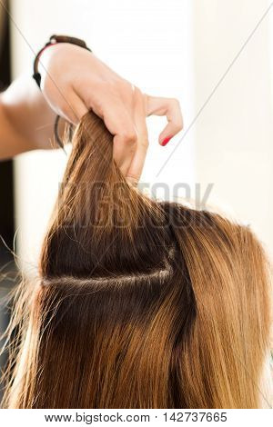 Close up view of hairdresser hand holding strand of hair preparing to cutting and dyeing hair. Haircare making new hairdo keratin restoration and hair therapy concept