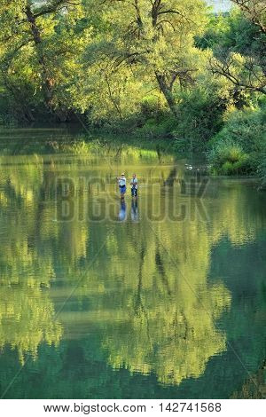 OVCAR BANJA, SERBIA - AUGUST 05, 2016: boy fishing under the watchful eye of his father in Morava River that flows in the lush green of Ovcar Gorge