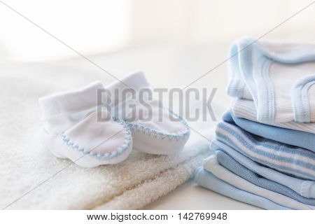 clothing, babyhood, motherhood and object concept - close up of white baby bootees, towel and pile of clothes for newborn boy