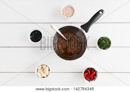 Cooking sauce for seafood, white wooden background. Tasty gravy in pan with spoon on table with variety of ingridients. Mediterranean cuisine, lusury restaurant food