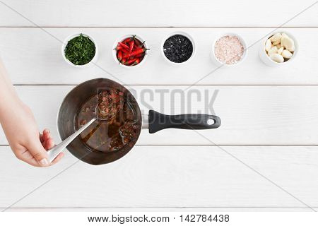 Cooking sauce for seafood, white wooden background. Hand mixing tasty gravy in pan on table with variety of ingridients. Mediterranean cuisine, lusury restaurant food