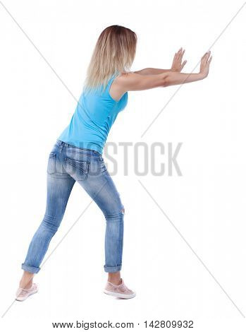 back view of woman pushes wall.  Isolated over white background. Rear view people collection. backside view of person. The blonde in a blue shirt and jeans, put her hands on the wall.