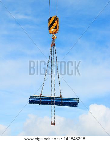 Yellow crane hook lifting load over clouds on blue sky. Construction industry background. 