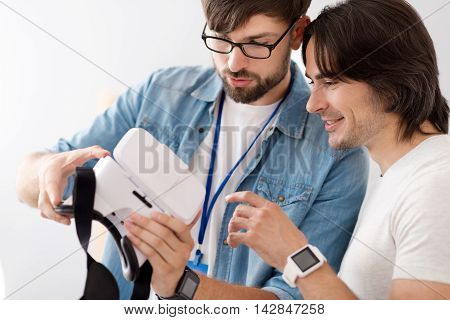 Look here. Positive diligent colleagues holding virtual reality glasses while working together