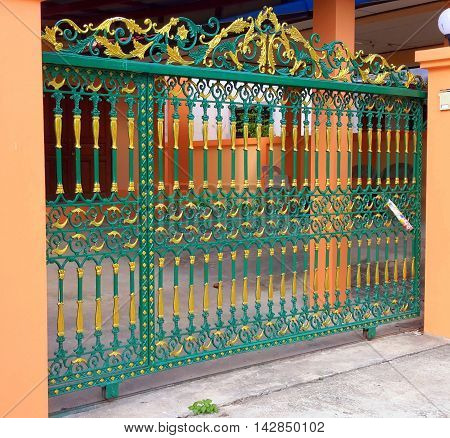 green and gold colored ornamental wrought iron gate on rollers, with peach colored gate posts, Songkhla, Thailand