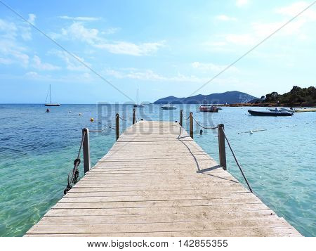 Wooden gangplank or jetty into the sea, with boats and blue sky.