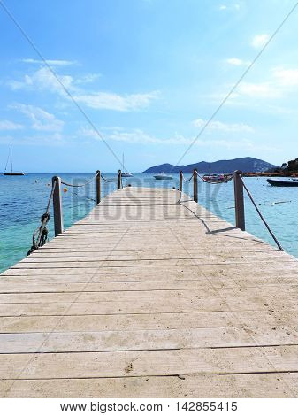 Wooden gangplank or jetty into the sea, with boats and blue sky.