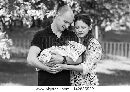 Happy Couple Holding Their Newborn Daughter In Her Arms. Outdoors.black And White Photography