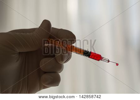 Person with latex glove pushes syringe drop hanging on the needle