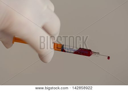 Person with latex glove pushes syringe drop at the injection needle