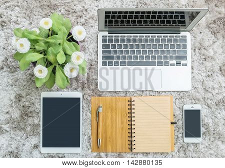 Closeup brown note book brown pen computer notebook tablet phone and artificial plant with white flower on gray fabric capet textured background in top view