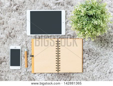 Closeup brown note book brown pen computer notebook tablet phone and artificial plant on gray fabric capet textured background in top view in work concept