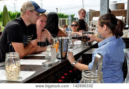 Middletown Rhode Island: Bar tender pouring a bottle of white wine for a young couple to taste at the Newport Winery Vineyard