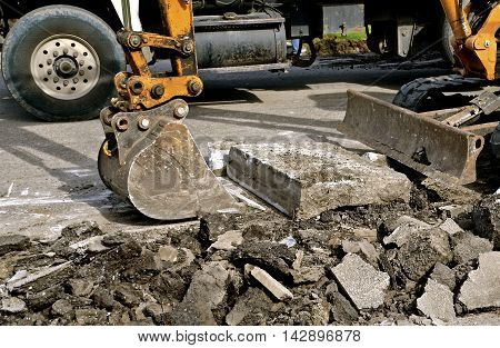 A backhoe picks up concrete slab in a demolition curbside project in a hydraulic bucket.