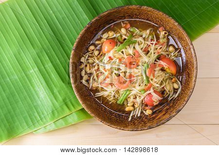 papaya salad (papaya pok pok) top view on a wooden table and green banana leaf Thai local food.
