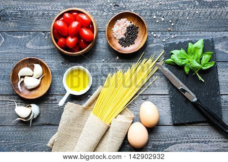 Top view of italian ingredients for tomato and basilic spaghetti with olive oil and garlic over a wood background.