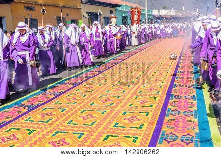 Antigua Guatemala - March 25 2016: Locals reenact biblical scenes walking over handmade dyed sawdust carpets on Good Friday in colonial town with most famous Holy Week celebrations in Latin America.