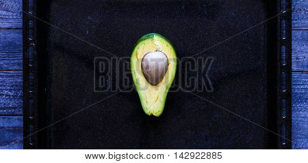 Veggie Food composition with half avocado over a darkdish and a wood distressed old background. Dramatic light.