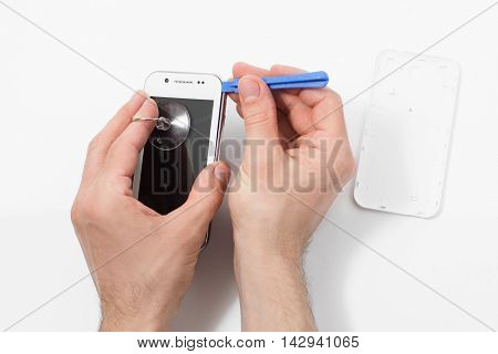 Smartphone disassembling with special tools. Phone repair service, male hand removing plastic case from communication device, white background