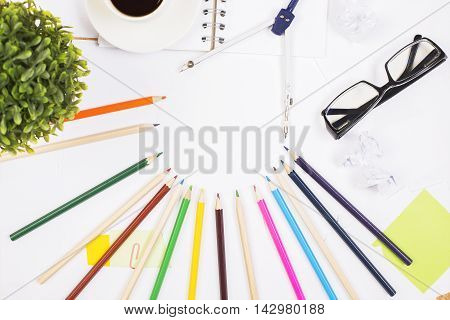 Top view of creative white desktop with colorful pencils glasses coffee cup plant pair of compasses and other items