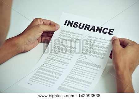 closeup of a young caucasian man sitting at a white table reading the terms of an insurance
