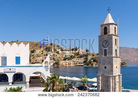 Symi, Greece - May 15, 2018: Clock Tower Symi And Blue Sea. Symi Island, Greece