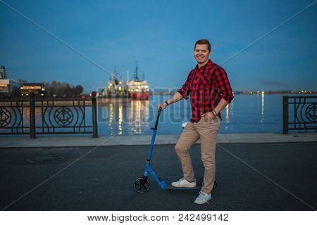 Young Handsome Guy Posing With Kick Scooter By Night Street Background.