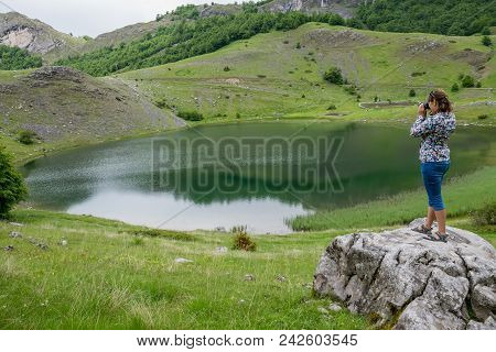A Girl Photographer Takes A Picture Of A Lake Standing On A Large Rock.