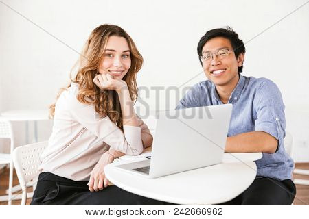 Happy multhiethnic business couple working on laptop computer while sitting indoors